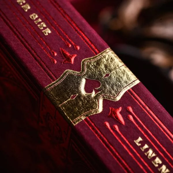 Close-up of gold decorative detailing and a spade symbol on a burgundy playing card box
